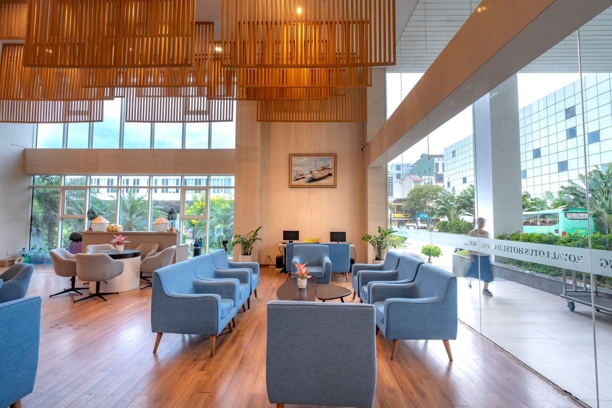 Recepção clara de hotel, com poltronas azuis, madeira e entrada de vidro