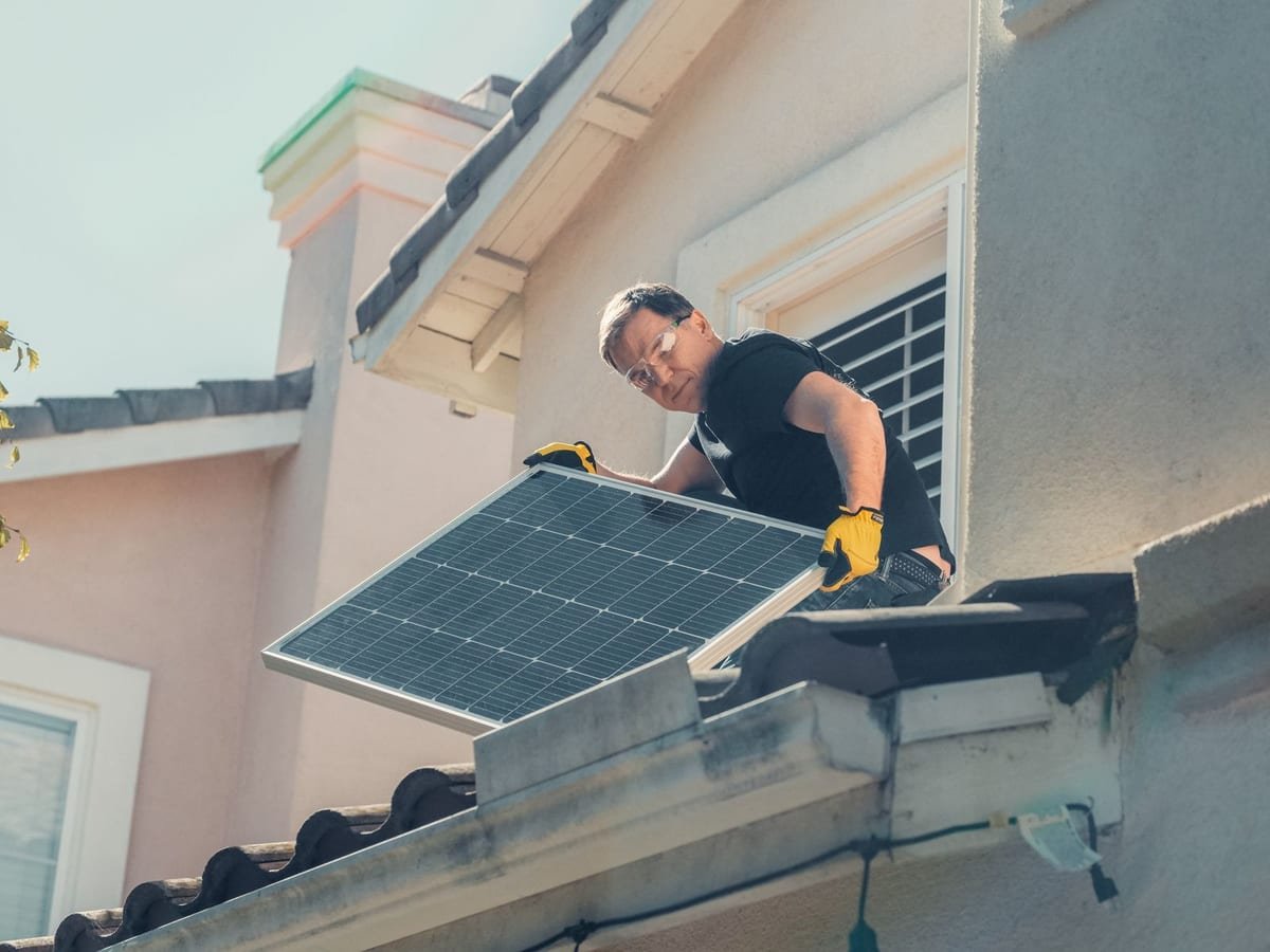 Trabalhador de óculos de proteção e luvas manuseando um módulo fotovoltaico no telhado