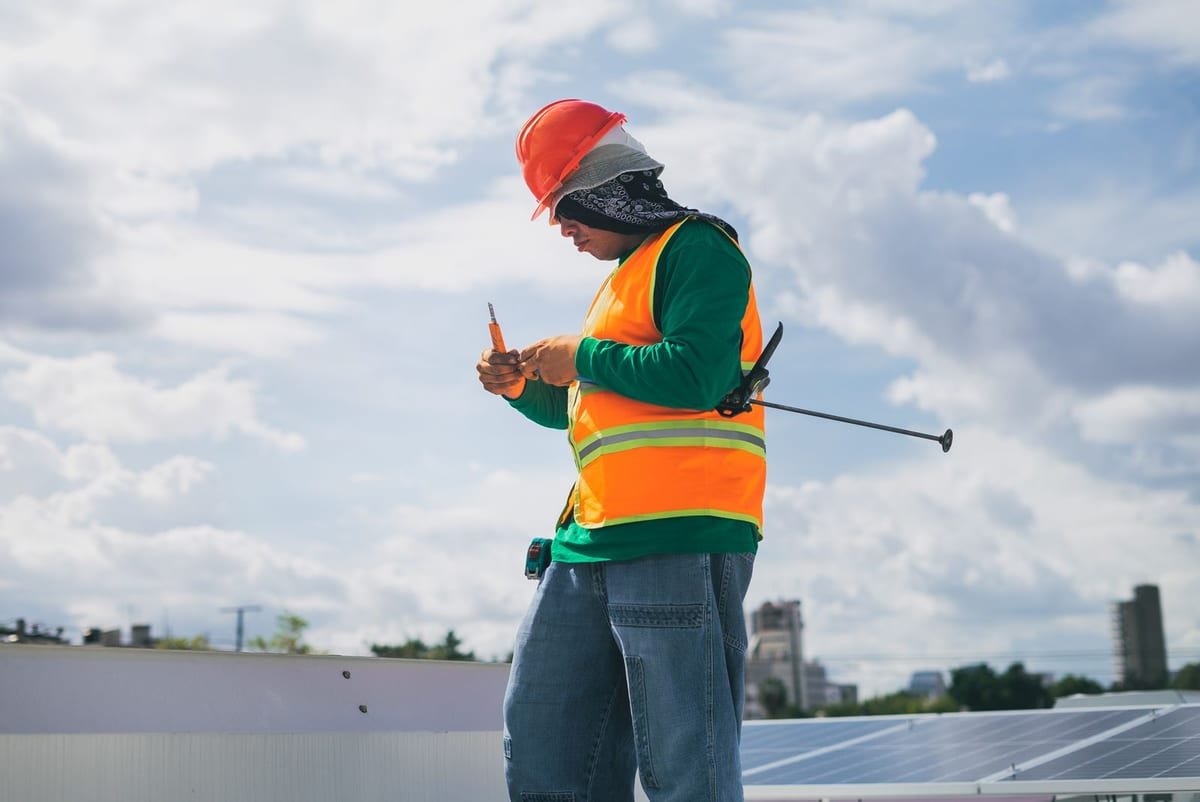 Profissional trabalhando em cima de um telhado com módulos fotovoltaicos, visto de baixo